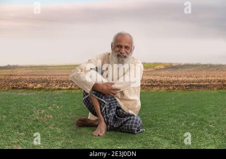 AN OLD FARMER HAPPILY SITTING ON GRASSLAND Stock Photo