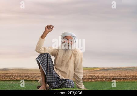 A TURBANED OLD VILLAGE MAN SITTING ON FARMLAND AND HAPPILY THINKING Stock Photo