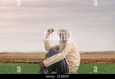 A HAPPY FARMER SITTING ON A FIELD AND LOOKING ABOVE Stock Photo