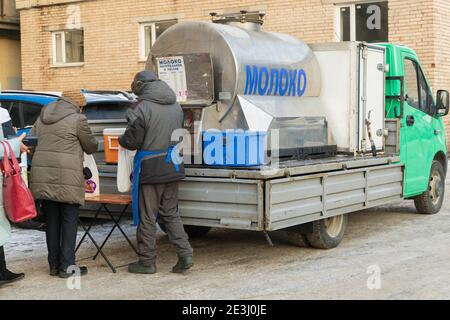 Saint Petersburg, Russia - January 09, 2021: Seller and buyers of farm milk near the tank with the inscription in Russian 'Milk' Stock Photo