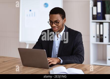 Young black entrepreneur working with laptop, office interior Stock Photo