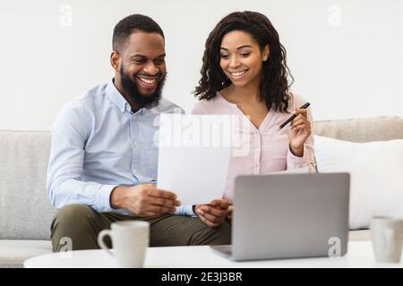 Cheerful black couple reading documents at home, checking agreement Stock Photo