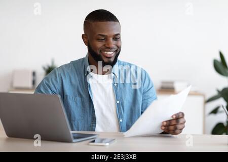 Millennial Black Freelancer Man Working With Papers At Desk In Home Office Stock Photo