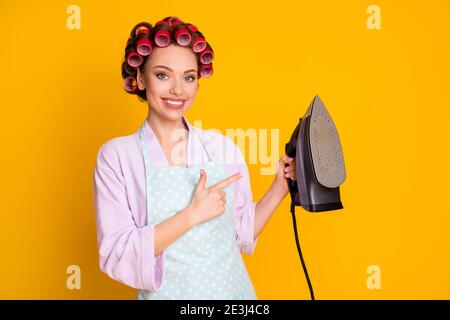 Portrait of lovely cheery maid holding in hand demonstrating new modern iron steam isolated bright orange color background Stock Photo
