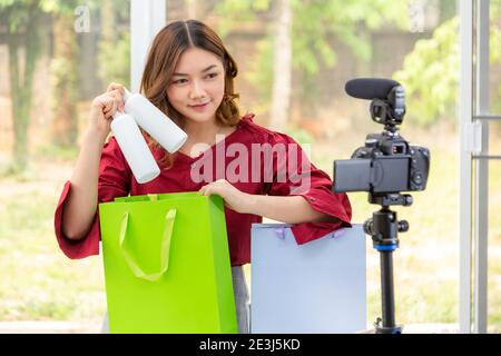 Beautiful young Asian woman, vlogger, smiling at her camera while putting the beauty product bottles in the bag after reviewing the products on her vi Stock Photo