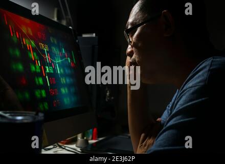 Close up Asian middle-aged man analyzing the candlestick graph chart of stock market investment trading seriously from computer in his room at night. Stock Photo