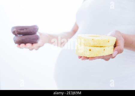 Pregnant woman hesitating between donuts and slices of pineapple Stock Photo