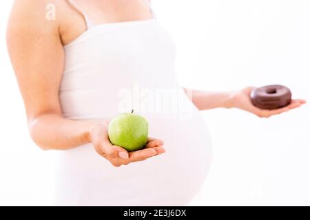 Pregnant woman choosing healthy apple over unhealthy donut on white background Stock Photo