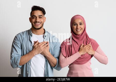 Grateful muslim couple keeping both hands on chest, expressing gratitude and appreciation Stock Photo