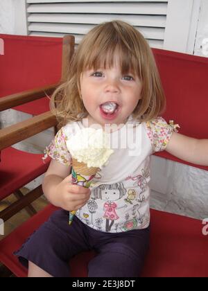 Toddler sat on chair eating an ice-cream cone Stock Photo