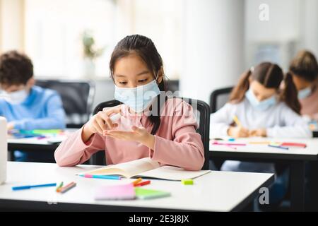 Small asian student applying antibacterial sanitizer on hands Stock Photo