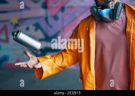 Graffiti artist throw his spray paint can against colorful graffiti on wall. Street art and contemporary painting process Stock Photo