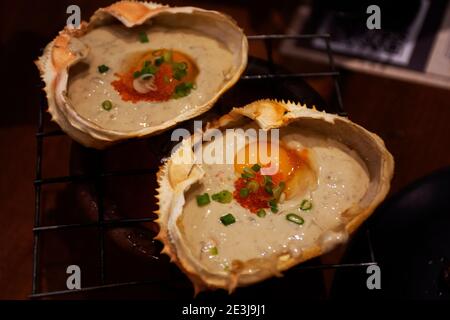 Famous Kani Miso or Crab Paste with soybeans with salt japanese seasoning topping quail eggs in Crab Shell grilled roasted on small coal stove at cafe Stock Photo