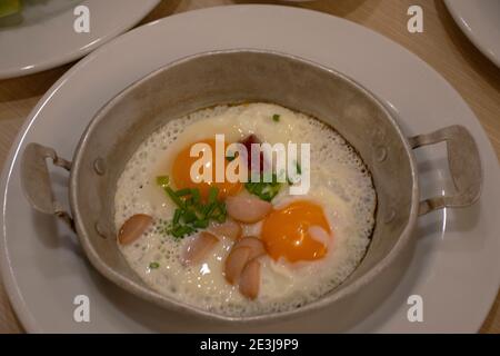 Food set of breakfast pan-fried egg with toppings sausage and vegetables on small pan at local restaurant in Udonthani city at morning time in Udon Th Stock Photo