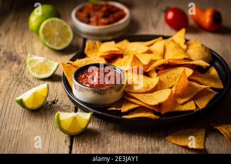 Single big black plate of yellow corn tortilla nachos chips with salsa sauce over wooden table Stock Photo