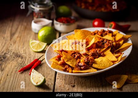 Delicious plate of yellow corn nachos chips with cheese, minced meat and red hot spicy salsa over wooden table Stock Photo