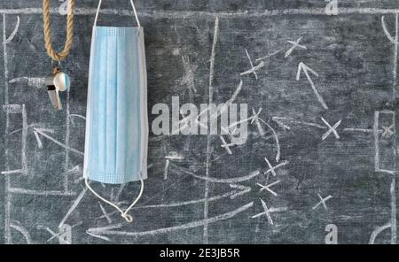 Soccer in times of COVID-19, referee whistle and corona mask on black board with tactical diagram, sport and social distancing concept Stock Photo