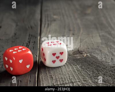 Two red and white dices with hearts on dark wooden background. Copy space.  Stock Photo
