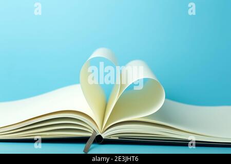 Heart made from white pages of notepad on a blue desktop background. Stock Photo