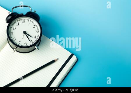 Notepad for sticky notes on desktop with alarm clock. Office desktop, management and timing concept. Stock Photo