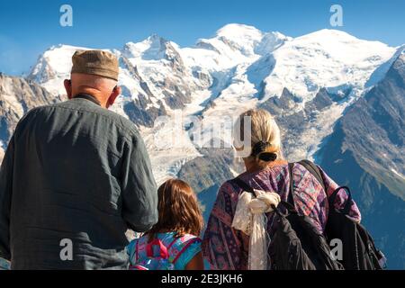 Family holidays in mountains. Senior man and woman with their granddaughter admiring snow cover Mont Blanc mountain in Alps. Back view. Elderly wellne Stock Photo