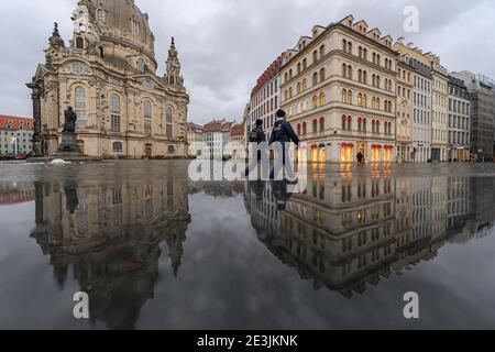 Dresden, Germany. 19th Jan, 2021. The Frauenkirche and the houses on the Neumarkt are reflected in a wet stone bench in the afternoon while two employees of the police department (Ordnungsamt) walk along. Credit: Robert Michael/dpa-Zentralbild/dpa/Alamy Live News Stock Photo