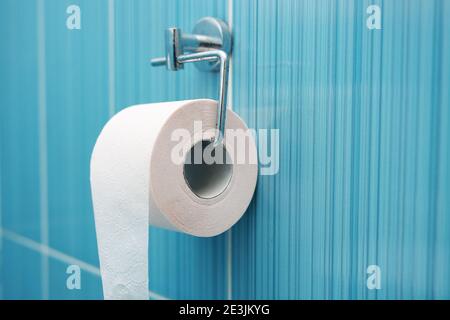 A roll of toilet paper hangs on a metal holder against a blue tile wall.  Stock Photo