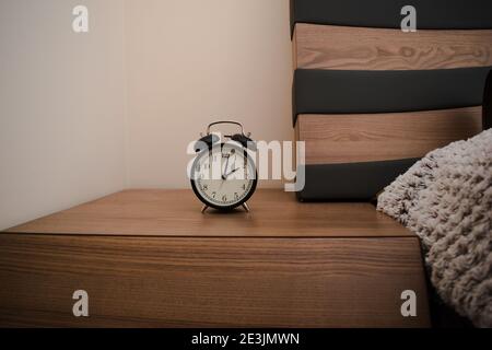 Old vintage alarm clock on a bedside table in bedroom. Retro analog twin bell alarm clock.Still life. Stock Photo