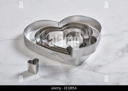 Set of stainless steel heart-shaped cookie cutters on a white marble surface Stock Photo