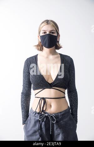 A nineteen-year-old calm girl with a bob hairstyle and bleached strands in a gray top with lurix and gray wide pants with a black medical mask on her Stock Photo