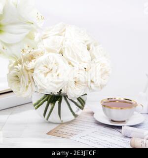 White roses, lily, in round vases with two cups of coffee on the table for a special occasion as a kitchen decoration. Copy space Stock Photo