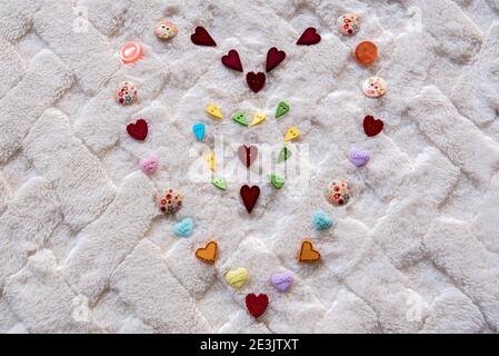 Multi-colored heart design on a soft white blanket.  Design is mostly made from heart shaped buttons. Stock Photo