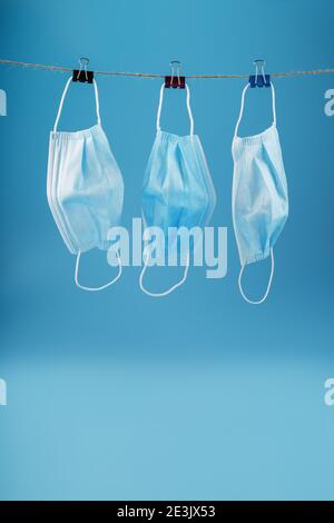 Three surgical masks hang on a clothesline against a blue background. Free space Stock Photo