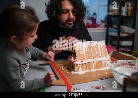 Father and daughter building gingerbread house at kitchen table Stock Photo