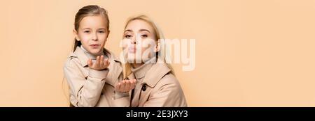 mother and daughter in trench coats sending air kisses isolated on beige, banner Stock Photo