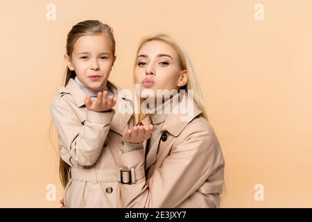 mother and daughter in coats sending air kisses isolated on beige Stock Photo