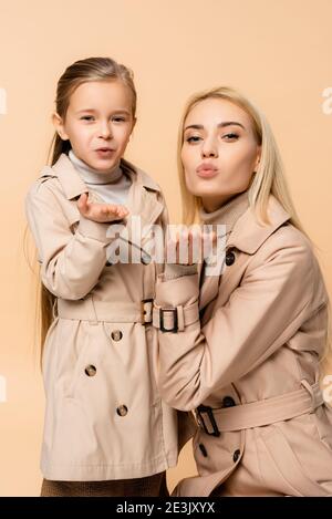 mother and daughter in trench coats sending air kisses isolated on beige Stock Photo