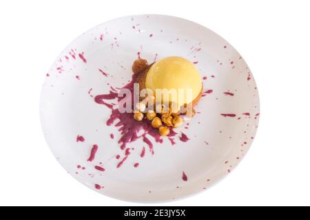 Yellow mousse with hazelnut lies on a plate. This dessert lies on a blot of fruit sauce. Isolated in a whte background. Close-up. Stock Photo