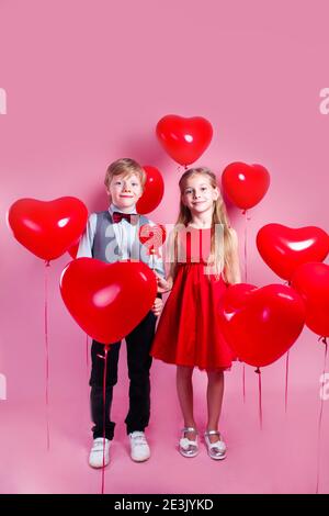 Valentines day. Two happy kids with red heart balloons on a pink background Stock Photo