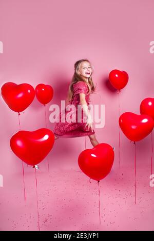 Valentines day. Little cute girl jumping with red heart balloons on pink background Stock Photo