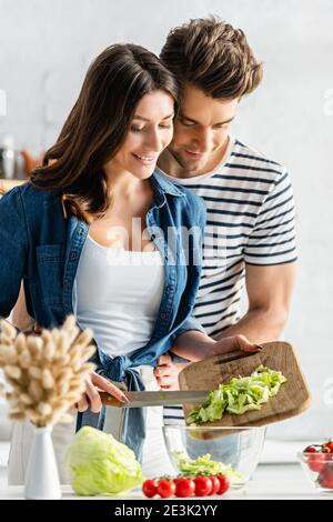 cheerful couple preparing salad in kitchen with catkins on blurred foreground Stock Photo