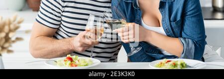 partial view of couple toasting glasses of wine near plates with salad in kitchen, banner Stock Photo