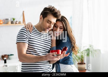 surprised man looking at heart-shaped gift box near happy girlfriend Stock Photo