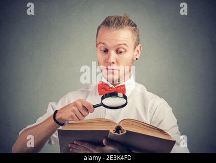 Portrait of a young man reading an interesting book with magnifying glass Stock Photo