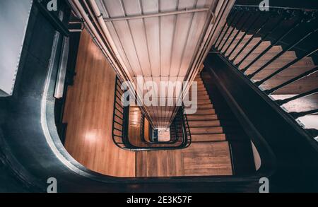 Wide-angle view from the top of a long stairwell going down in a helix in an antique house with a metal railing and a lift shaft in the center, select Stock Photo