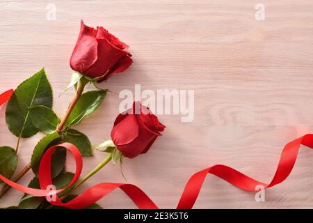 Romantic background with two red roses and red ribbon on wood table. Top view. Stock Photo