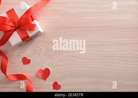 Romantic background with white gift with bow and heart-shaped cutouts on wooden table. Top view. Stock Photo