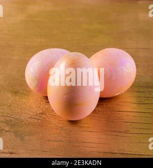 Three Easter eggs colored in pink and gold on old wooden cracked golden surface. Stock Photo