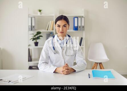 Young general practitioner looking at camera while sitting at table in her office Stock Photo