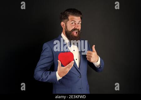 Fall in love. Celebrate love. Trust me. Happy valentines day. Tuxedo man hold red heart. Love concept. Passionate mature lover hipster in formal suit. Businessman with bow tie. Romantic greeting. Stock Photo